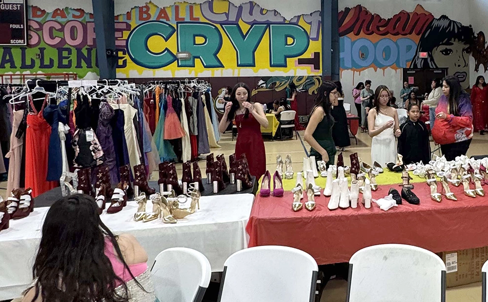 View of the all purpose room with dresses hanging on racks, shoes lined up on tables, young women trying on dresses and getting ready