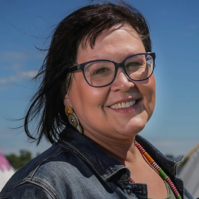 Smiling Native woman wearing glasses, beaded earrings, necklace and denim shirt