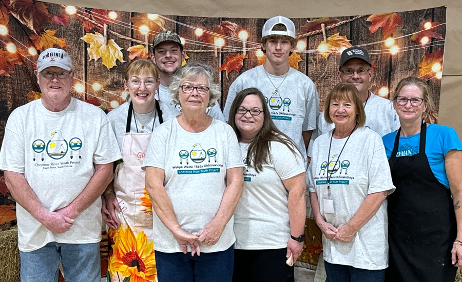 Group of mixed-age people wearing CRYP tshirts smiling in front of a harvest-themed background.