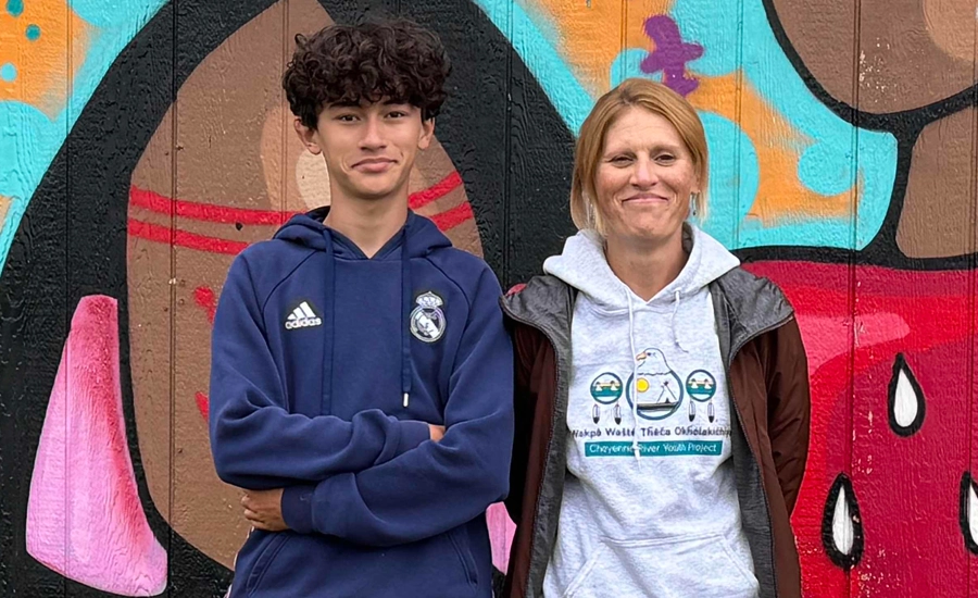 Teenaged youth and adult woman wearing CRYP sweatshirt and smiling in front of colorful outdoor art mural.