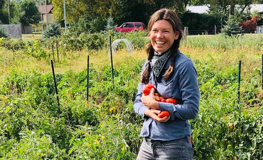 CRYP Volunteer_Shayne Case Caucasian woman with long brown hair braided smiles in the garden holding an arm load of ripe tomatoes.