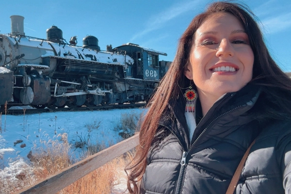 Woman with long brown hair smiling in front of an antique locomotive.