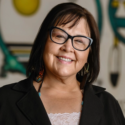 Smiling Native woman wearing glasses, beaded earrings, necklace and denim shirt